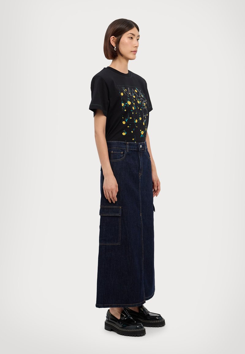 Zwarte t-shirt met een kleurrijke grafische print, gecombineerd met een lange spijkerrok met opgestikte zakken, en zwarte platform schoenen.