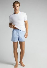 White fitted t-shirt and blue and white striped boxer shorts. Shorts have an elastic waistband, and both garments are made of soft fabric.
