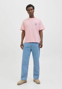 Rosa bomulds T-shirt med korte ærmer og et grafisk print på brystet, parret med lyseblå denim jeans og beige slip-on sko.