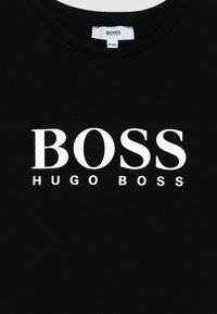 Camiseta de algodón negra con cuello redondo y un audaz logo impreso en blanco "BOSS HUGO BOSS" en el frente, con una tipografía limpia y moderna.