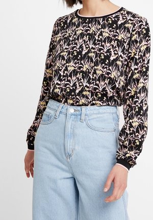 Maglietta nera a maniche lunghe con un motivo floreale in rosa e giallo; colletto a girocollo, polsini elasticizzati. Abbinata a jeans a vita alta in denim chiaro.