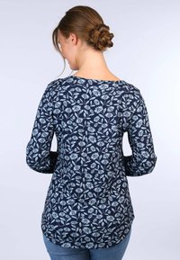 Himmelblaues Langarmoberteil mit Blumenmuster in hellblau, rundem Halsausschnitt und geschwungener Saumlinie. Weicher, strukturierter Stoff.