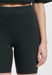 Donkergroene fietsbroek gemaakt van rekbaar materiaal met een hoge tailleband. Kenmerkt zich door een gladde textuur en een aansluitend ontwerp.