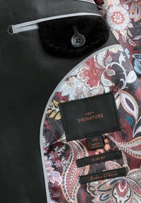 Sort stofjakke med paisley-mønstret foer. Har en elegant lomme og grå detaljer. Mærkerne inkluderer "NEXT SIGNATURE" og "Slim Fit."