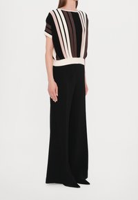 Svarta vida byxor med en åtsittande, randig topp i kräm, rosa och nyanser av brunt. Mjuk, lättviktsmaterial med en avslappnad passform.