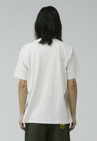 White cotton short-sleeve t-shirt with a relaxed fit, featuring a tag on the lower left side and a smooth texture.