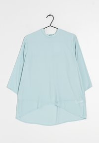 Blouse bleu clair à manches longues avec un col rond, fabriquée en tissu doux et lisse. Présente un ourlet asymétrique et une coupe décontractée. Accrochée à un crochet.