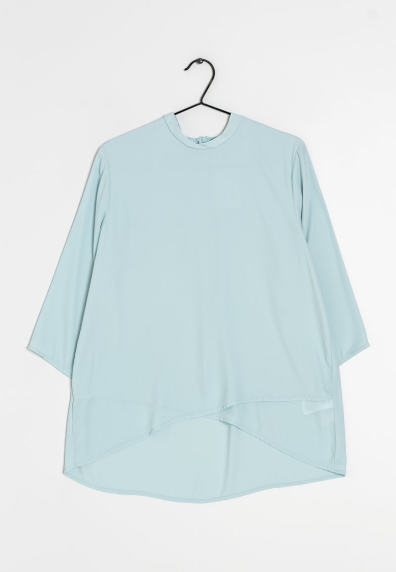 Blouse bleu clair à manches longues avec un col rond, fabriquée en tissu doux et lisse. Présente un ourlet asymétrique et une coupe décontractée. Accrochée à un crochet.