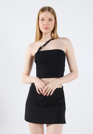 Top corto negro con un diseño de un solo hombro y correa ajustable. Combinado con una falda corta negra ajustada. Textura de tejido suave.