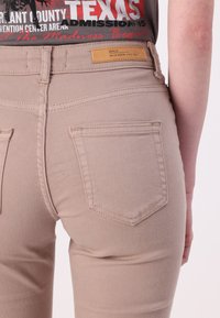 Jean en denim beige au design ajusté. Comprend deux poches arrière, des coutures ton sur ton et une étiquette sur la taille. Texture lisse.