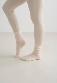Beige ribkované legíny s přiléhavým střihem, doplněné měkkými béžovými kotníkovými ponožkami s ohrnutým lemem, na světlé podlaze.