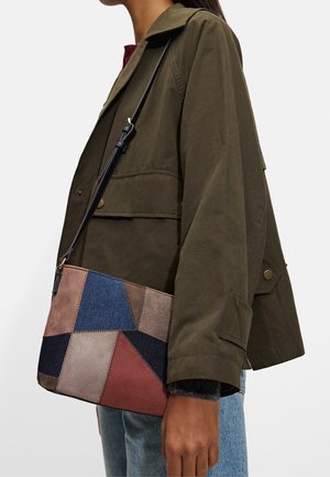 Mehrfarbige Patchwork-Handtasche aus Wildleder und Denim, mit geometrischen Formen in Blau, Braun, Pink und Schwarz, ausgestattet mit einem schwarzen Trageriemen.