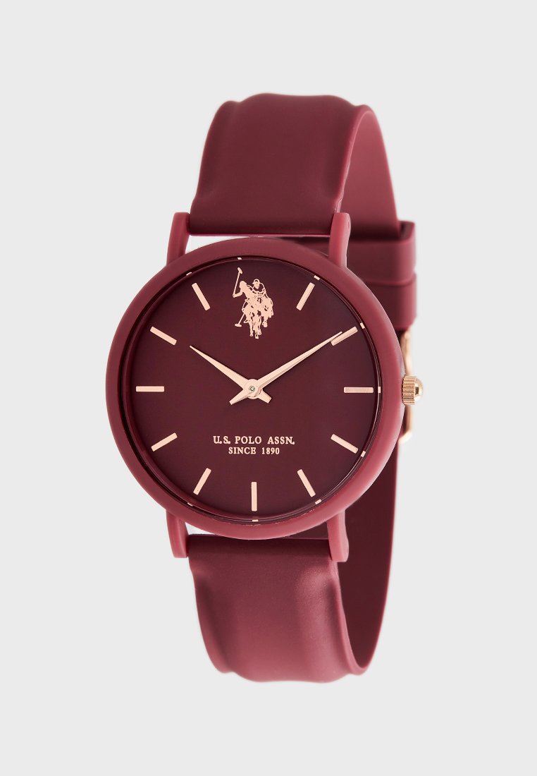 Burgunderfarbene Silikon-Uhr mit einem runden matten Zifferblatt. Goldfarbene Stundenmarkierungen und Zeiger, mit einem Polo-Spieler-Logo und Markennamen am unteren Rand.
