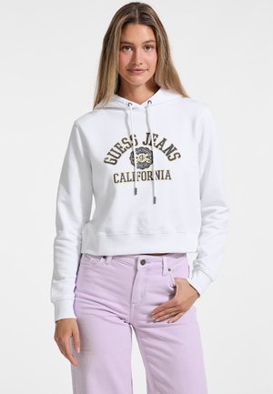 White cropped hoodie featuring a logo print in black and gold, paired with light purple jeans. The fabric is smooth with a soft texture.