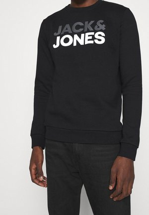 Czarna bluza z logo „JACK & JONES” w szaro-białych kolorach, noszona przez osobę widoczną od ramion do bioder.