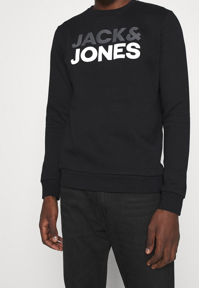 Sweat-shirt noir avec le logo "JACK & JONES" en gris et blanc, porté par une personne visible des épaules aux hanches.