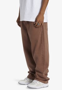 Bruna bomullscargobyxor med avslappnad passform, utrustade med sidfickor och en mjuk textur, kombinerade med vita sneakers med gråa accenter.