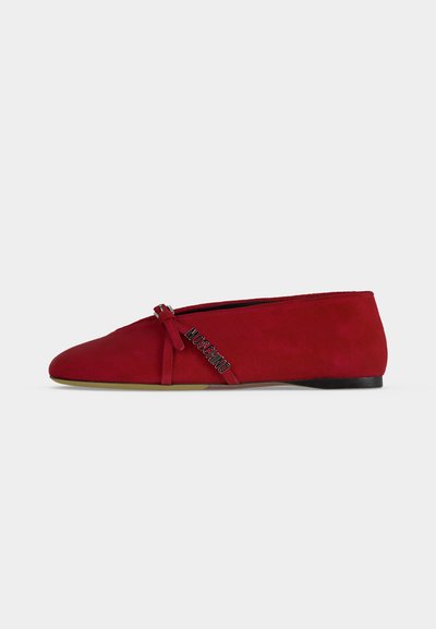 Chaussure plate en daim rouge avec bout pointu, détail nœud et logo Moschino argenté sur le côté, talon bas noir et semelle beige.