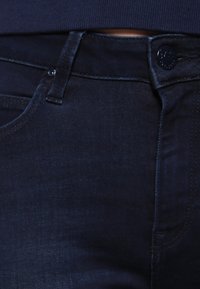 Mörka denimjeans med en slät textur, som har en klassisk femfickdesign, knäppning och subtila sömnadsdetaljer.