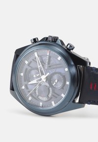 Montre chronographe noire avec un boîtier en métal bleu foncé, un cadran texturé, des aiguilles argentées et un bracelet en cuir avec des accents rouges.