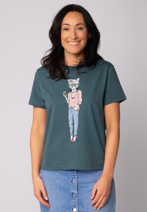 Teal katoenen T-shirt met korte mouwen, versierd met een afbeelding van een kat met een bril, gekleed in een roze top en jeans, met rode hoge hakken.