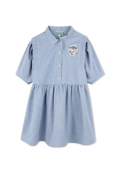 Robe en chambray bleu clair avec un devant à boutons, des manches courtes bouffantes et une jupe froncée. Présente un patch brodé avec logo sur la poitrine.
