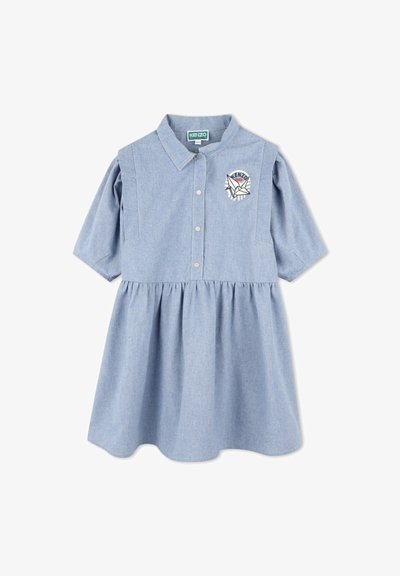 Robe en chambray bleu clair avec un devant à boutons, des manches courtes bouffantes et une jupe froncée. Présente un patch brodé avec logo sur la poitrine.