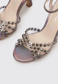 Sandales à talons transparents avec des sequins circulaires argentés, design à bout ouvert et bandeau fin à la cheville. Fini irisé sur la semelle.