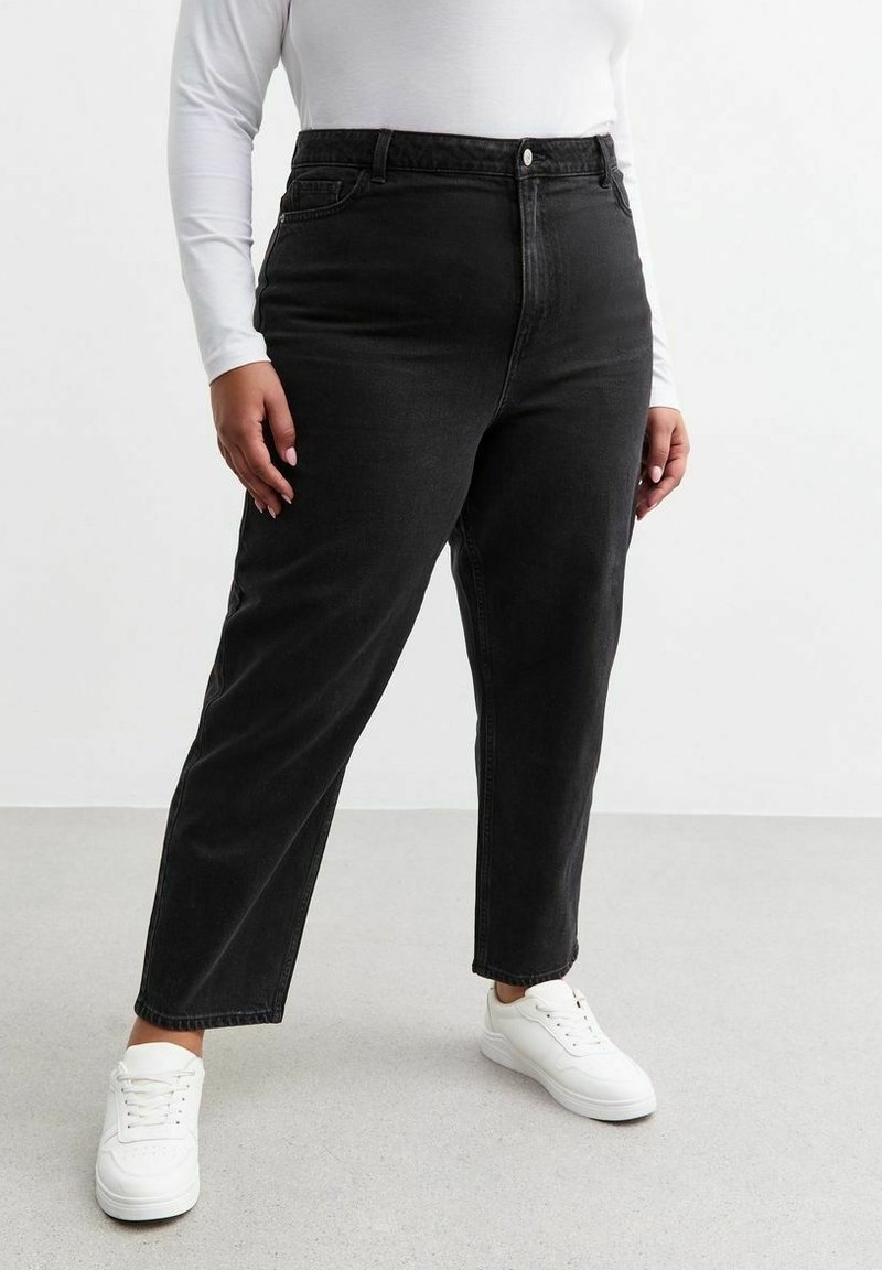 Vaqueros de mezclilla negros de tiro alto con un corte recto, diseño de cinco bolsillos y un ligero desgastado, combinados con zapatillas blancas.