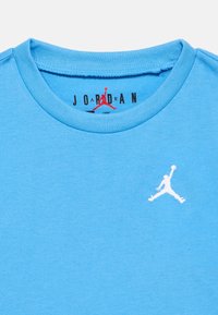 Ανοιχτό γαλάζιο βαμβακερό T-shirt με στρογγυλή λαιμόκοψη, που φέρει ένα λευκό κεντητό λογότυπο Jordan στο στήθος και την επιγραφή "JORDAN" σε μαύρο πάνω στην ετικέτα.