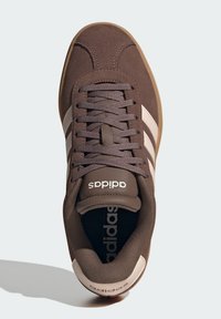  smeđa antilop tenisica s bijelim kožnim trakama, okruglim vrhom, ravnim vezicama i bež gumom. Ima Adidas logo na jeziku i unutrašnjosti.