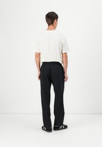 T-shirt blanc à manches courtes, pantalon à taille élastique noir, coupe décontractée, texture lisse, associé à des sandales noires avec des accents blancs.