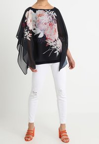 Svart genomskinlig topp med blommönster, vida ärmar, kombinerad med vita slitna jeans och orangea sandaletter med remmar.