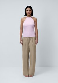 Rosa halter-top i en glatt stoff med en tettsittende silhuett, kombinert med beige, løstsittende bukser og sandaler med åpen tå.