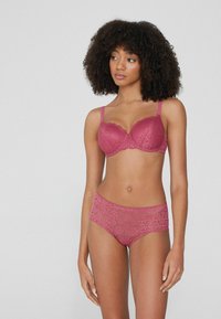 Różowy koronkowy stanik i dopasowane majtki z wysokim stanem mają kwiatowe wzory, falbany i regulowane ramiączka. Gładka tekstura i delikatny design.