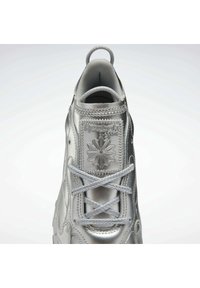 Silberfarbene, metallische Sneakers mit glatter Textur, ausgestattet mit dem Reebok-Logo, Schnürdesign und einer auffälligen Schlaufe an der Ferse für einfaches Anziehen.