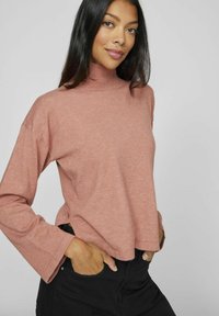 Sweter z golfem w kolorze brudnego różu, z długimi rękawami, luźny krój i prążkowany kołnierz. Połączony z czarnymi spodniami, prezentując casualowy styl i wygodę.