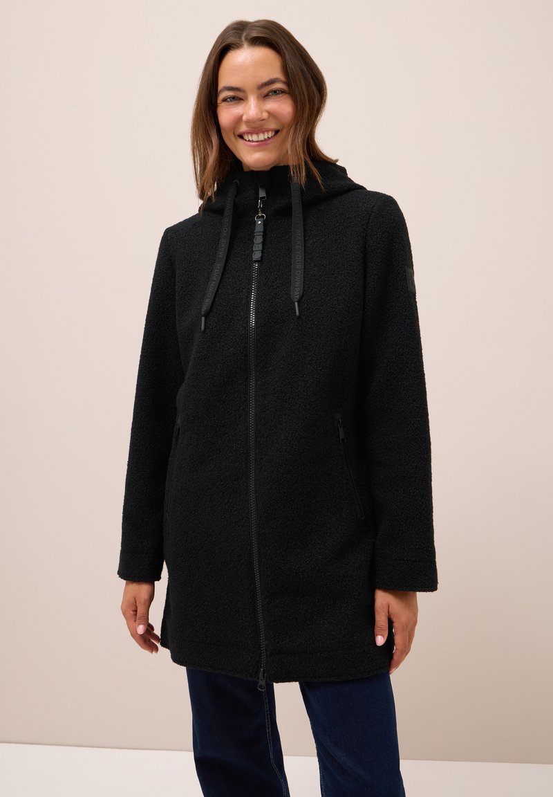 Manteau en polaire noir avec fermeture éclair à l'avant, capuche et cordons de serrage réglables, doté de poches latérales et d'un ourlet légèrement cintré.