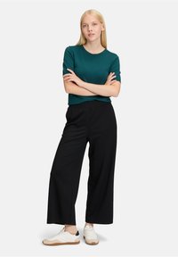 Teal kortemouwen gebreide top gecombineerd met losse zwarte broek en witte sneakers met een gumrubberen zool. Eenvoudige, casual outfit met minimale accenten.