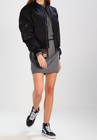 Giacca bomber nera con polsini a coste, abito in maglia grigia e sneakers alte nere e blu con lacci bianchi.