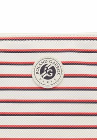 Borsa bianca con texture, caratterizzata da strisce orizzontali rosse e blu navy. Presenta un'etichetta circolare con il logo "Roland Garros Paris" al centro.