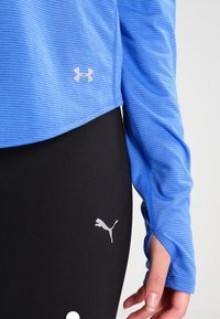 Vaaleansininen pitkähihaisessa paidassa on ribbitekstuuri ja hopeinen Under Armour -logo. Mustissa legginsseissä on valkoinen Puma-logo nilkan kohdalla.