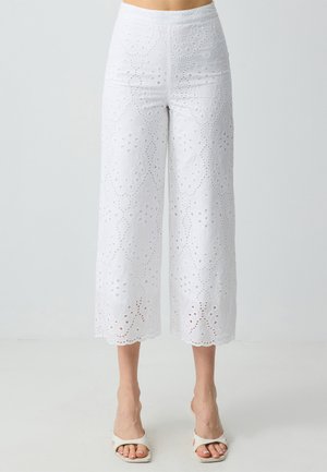 Pantaloni bianchi a 3/4 realizzati in cotone ricamato, caratterizzati da intricati motivi ritagliati, orlo a onde e una texture liscia.