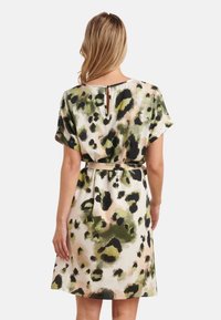 Kurzes Kleid mit lockerer Passform, das einen abstrakten grün-schwarzen Leopardenprint auf einem hellen Hintergrund zeigt. Mit einem Schlitzdetail im Rücken.