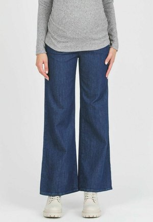Dunkelblaue, weite Jeanshosen mit einer glatten Textur, kombiniert mit hellfarbigen Schuhen. Sie weisen ein klassisches Design und eine neutrale Farbgebung auf.