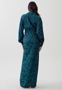 Lång mörk teal klänning med blommönster, elastisk midja och långa ärmar; tillverkad av ett slätt tyg med en lätt glänsande yta.