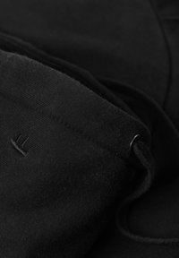 Tessuto di felpa nera con una morbida texture, caratterizzato da un piccolo logo ricamato e un dettaglio con cordino. Il colore è uniforme in tutta la superficie.
