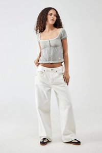 Γκρι μπλουζάκι με κοντά μανίκια, τετράγωνο ντεκολτέ και λεπτομέρειες με κουμπιά, συνδυασμένο με λευκά τζιν παντελόνια φαρδιάς γραμμής και μπλε παπούτσια με μπεζ λεπτομέρειες.