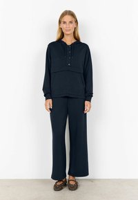 Dunkelblaue Kapuzenjacke mit einer Fronttasche, drei Knöpfen und Kordelzug. Kombiniert mit weit geschnittenen, passenden blauen Hosen. Texturiertes Material, lässige Passform.
