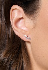 Srebrna klipsa do ucha z wzorem w zygzak, ozdobiona małymi, przezroczystymi kamieniami szlachetnymi, noszona na płatku ucha, podkreślająca swoje skomplikowane detale.